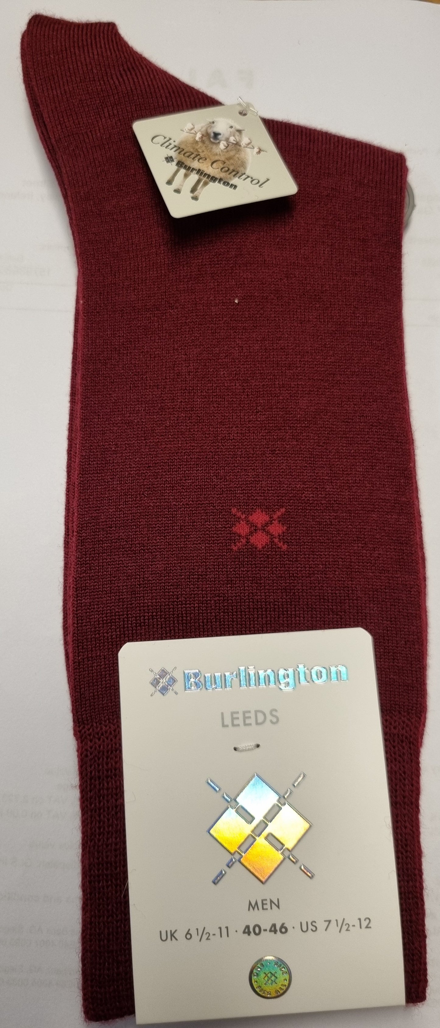 A single burgundy knit sock laid flat on a white sheet of paper, with a paper hangtag attached near the cuff and a larger size/brand card near the lower half. The sock has a small red embroidered cross logo and the brand name 'Bullington' is visible on the tag.