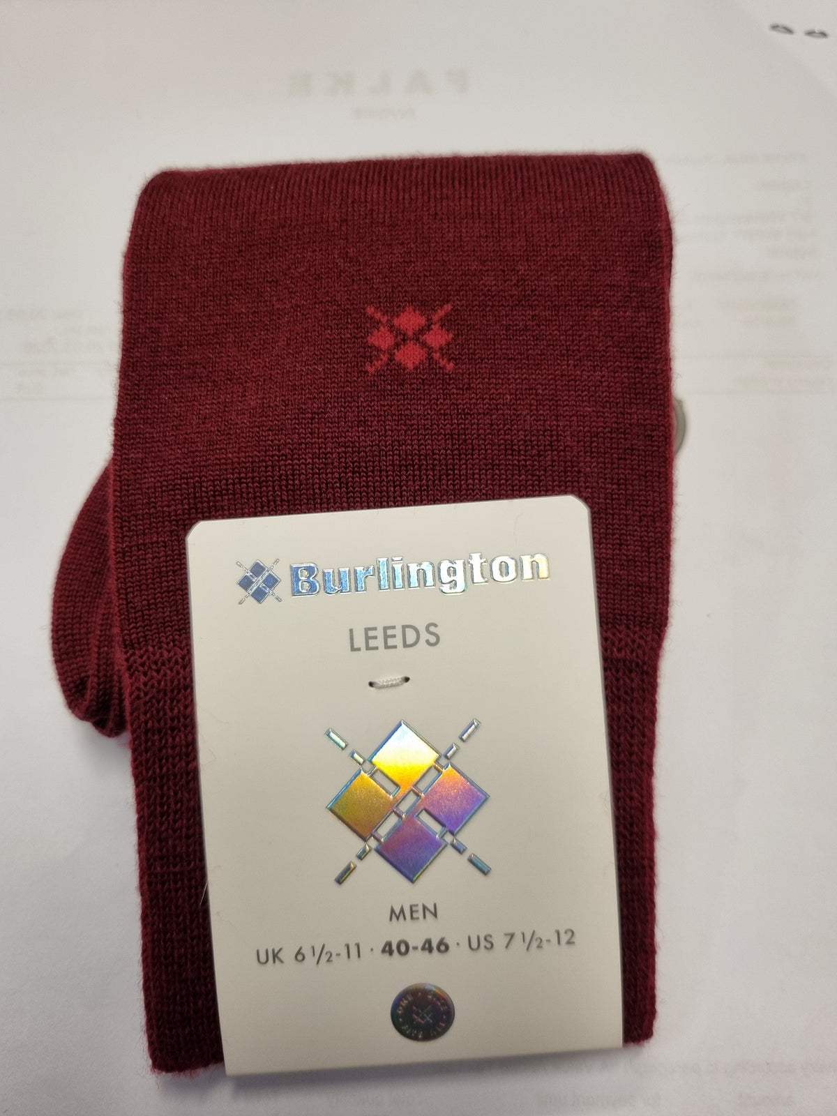 A folded pair of burgundy knit socks with a small red embroidered logo, attached to a white paper tag that reads 'Burlington LEEDS MEN'.
